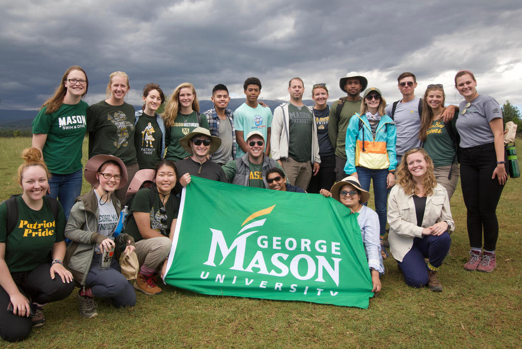 Grad and undergrad students gather for a group photo with a George Mason University Banner in Kenya